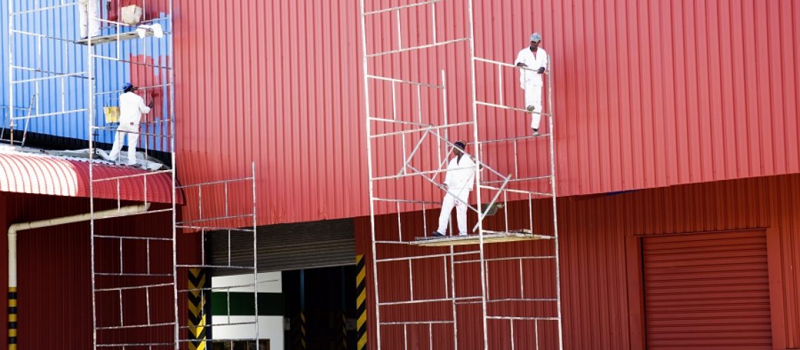 A team of industrial painters on scaffolding painting a roof facade.