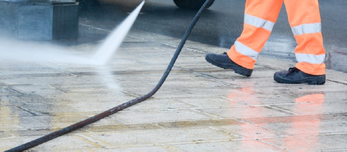 a dustman with a pressure washer cleaning the street
